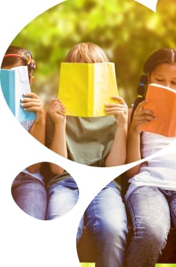 Children reading books at park against trees and meadow in the park